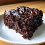 A single, delicious slice of fudgy zucchini brownies topped with chocolate chips on a white plate.