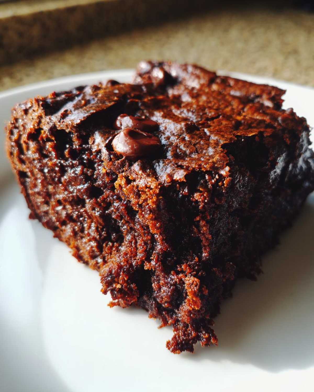 A single slice of fudgy zucchini brownies with chocolate chips on a white plate.