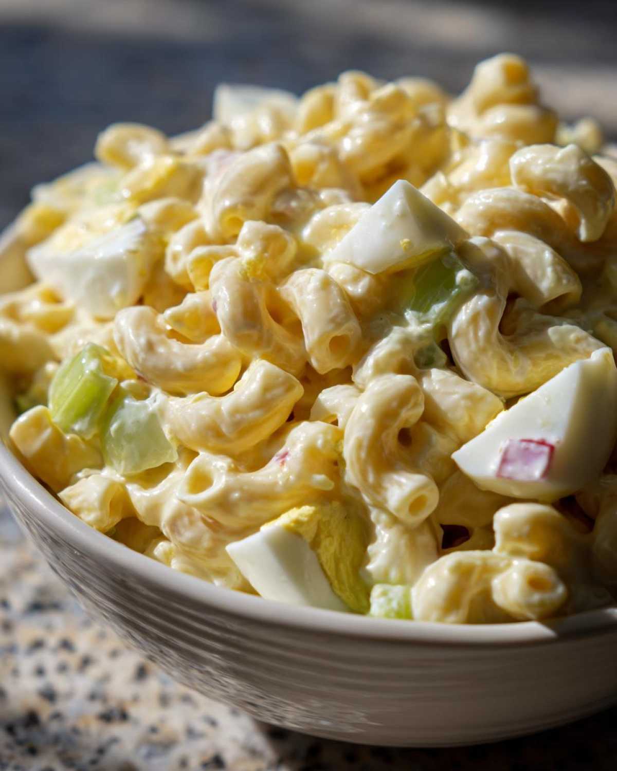 Close-up of a bowl of Amish macaroni salad with elbow pasta, hard-boiled eggs, celery, and creamy dressing.