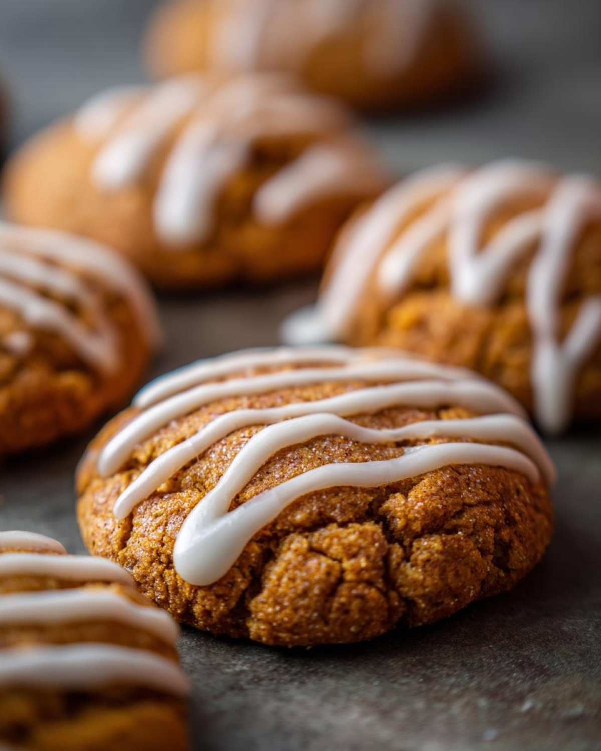 Close-up of glazed apple butter cookies on a gray surface. The cookies have a light brown color and white icing drizzle.