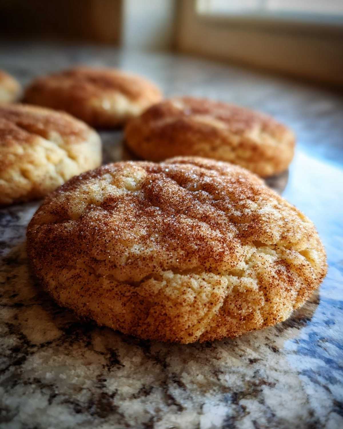 A close-up shot of several apple cider cookies, coated in cinnamon sugar, on a marble surface.