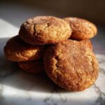 A stack of chewy apple cider cookies coated in cinnamon sugar on a marble surface.