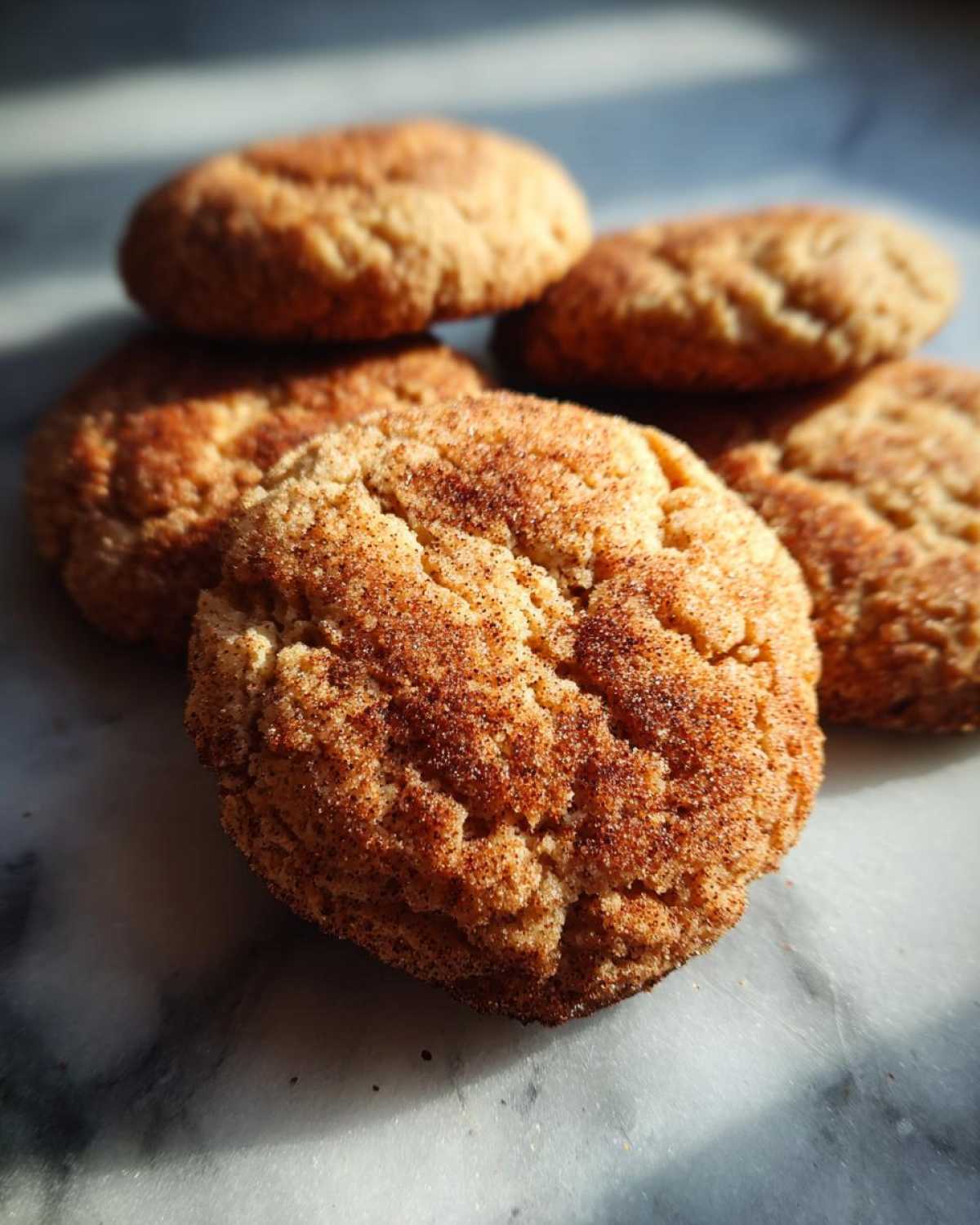A stack of freshly baked apple cider cookies, dusted with cinnamon sugar, on a marble surface.