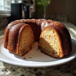 A delicious apple cider donut cake, sliced and served on a white plate, showcasing its moist texture.