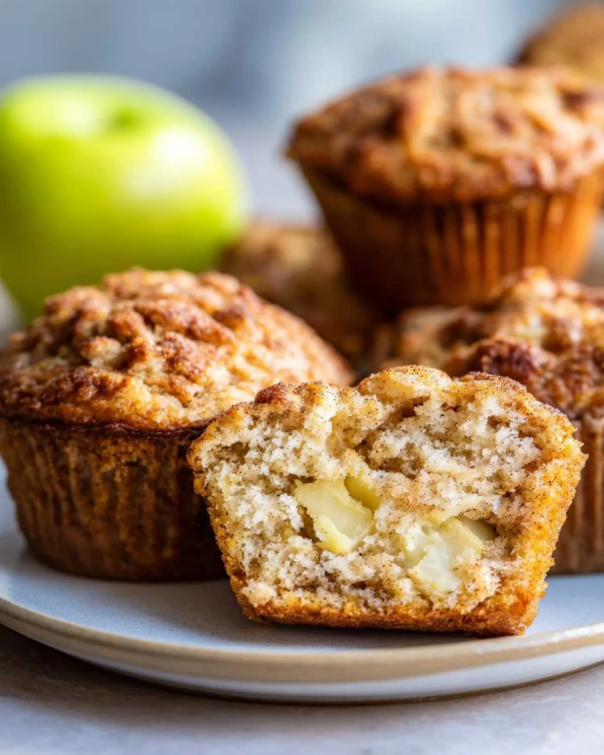 Close-up of apple muffins on a plate, one muffin cut in half to show the apple pieces inside.