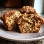 A halved apple muffin on a plate, showcasing the apple filling and crumbly topping. Delicious apple muffins.