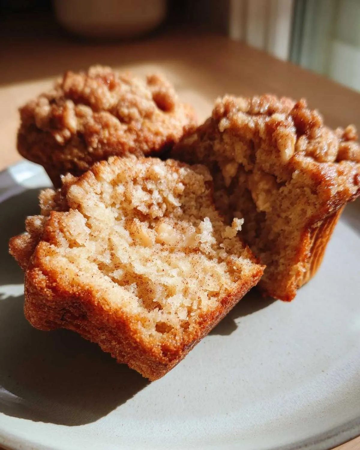 Three apple muffins on a plate, one muffin is cut in half to show the inside texture.