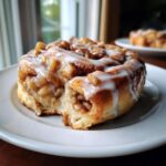 Close-up of an apple pie cinnamon roll with a bite taken out, showing the apple filling and glaze.