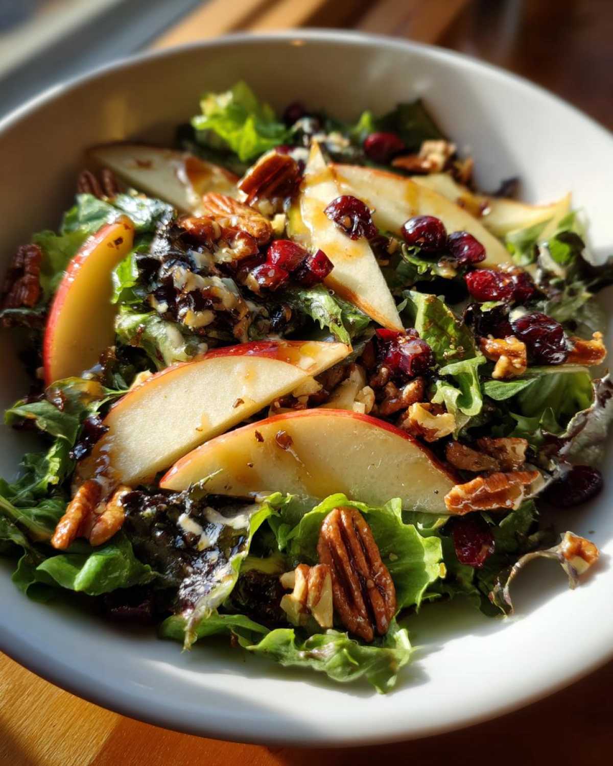 A vibrant autumn salad featuring mixed greens, apple slices, pecans, cranberries, and a balsamic vinaigrette dressing.