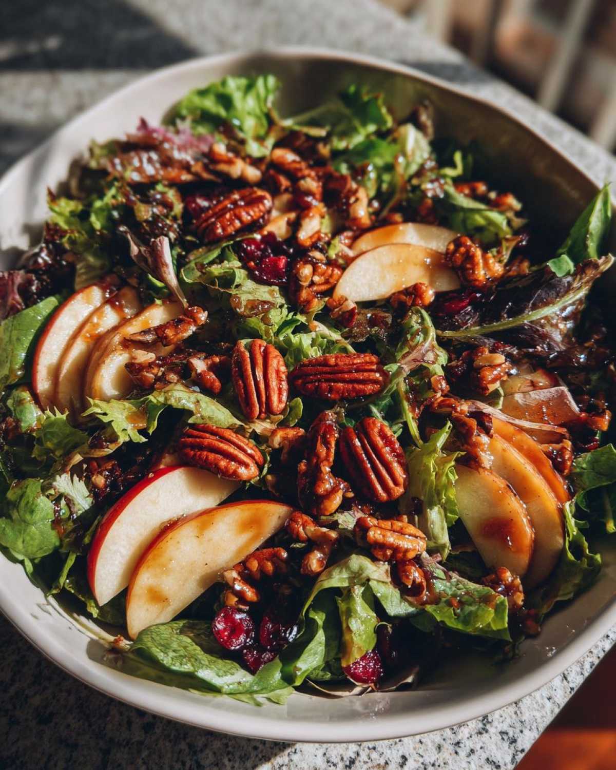 Overhead shot of a vibrant autumn salad with mixed greens, apple slices, pecans, and cranberries.