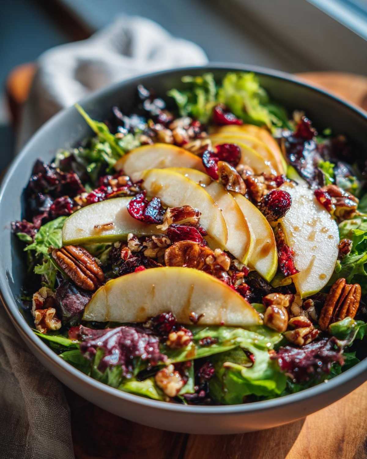 A vibrant autumn salad featuring mixed greens, sliced pears, pecans, and cranberries in a gray bowl. Delicious autumn salad.
