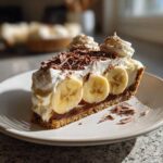 A slice of banoffee pie topped with bananas, whipped cream, and chocolate shavings.