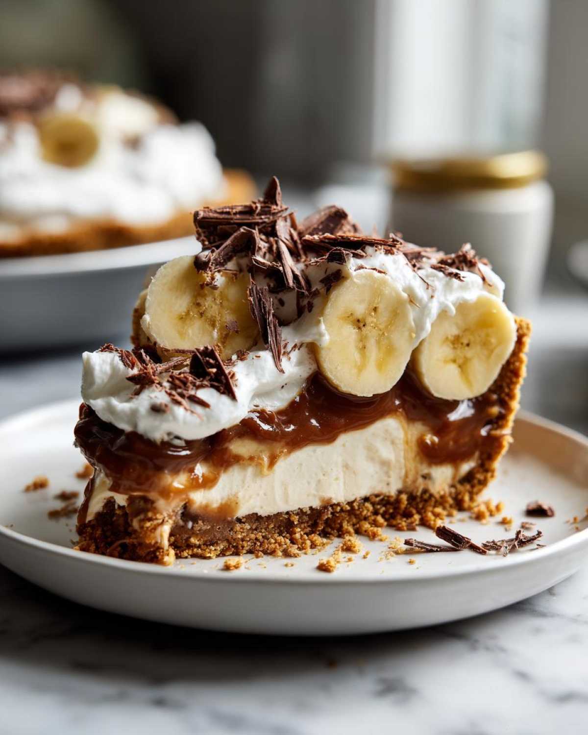 A slice of banoffee pie topped with bananas, whipped cream, and chocolate shavings.