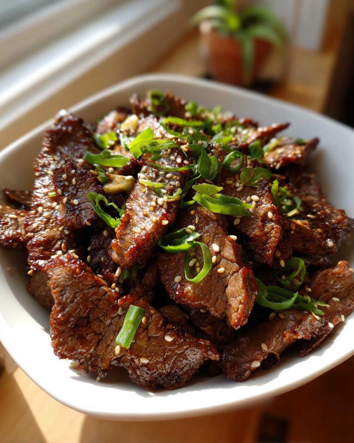 Close-up of a bowl of Bulgogi recipe, garnished with sesame seeds and green onions.