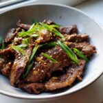 Bowl of Bulgogi recipe, garnished with sesame seeds and green onions, ready to eat.