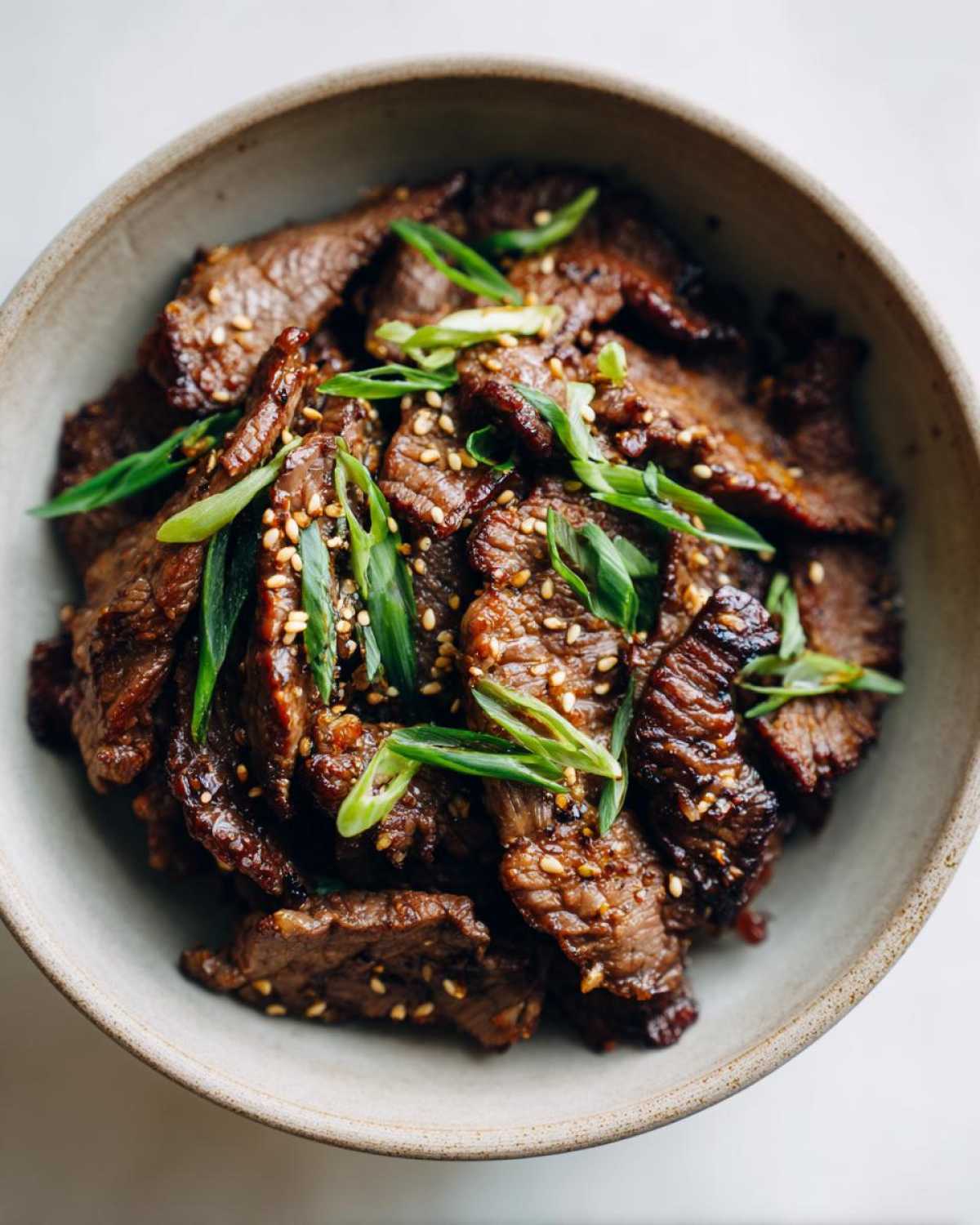 Close-up of Bulgogi recipe in a bowl, garnished with green onions and sesame seeds.