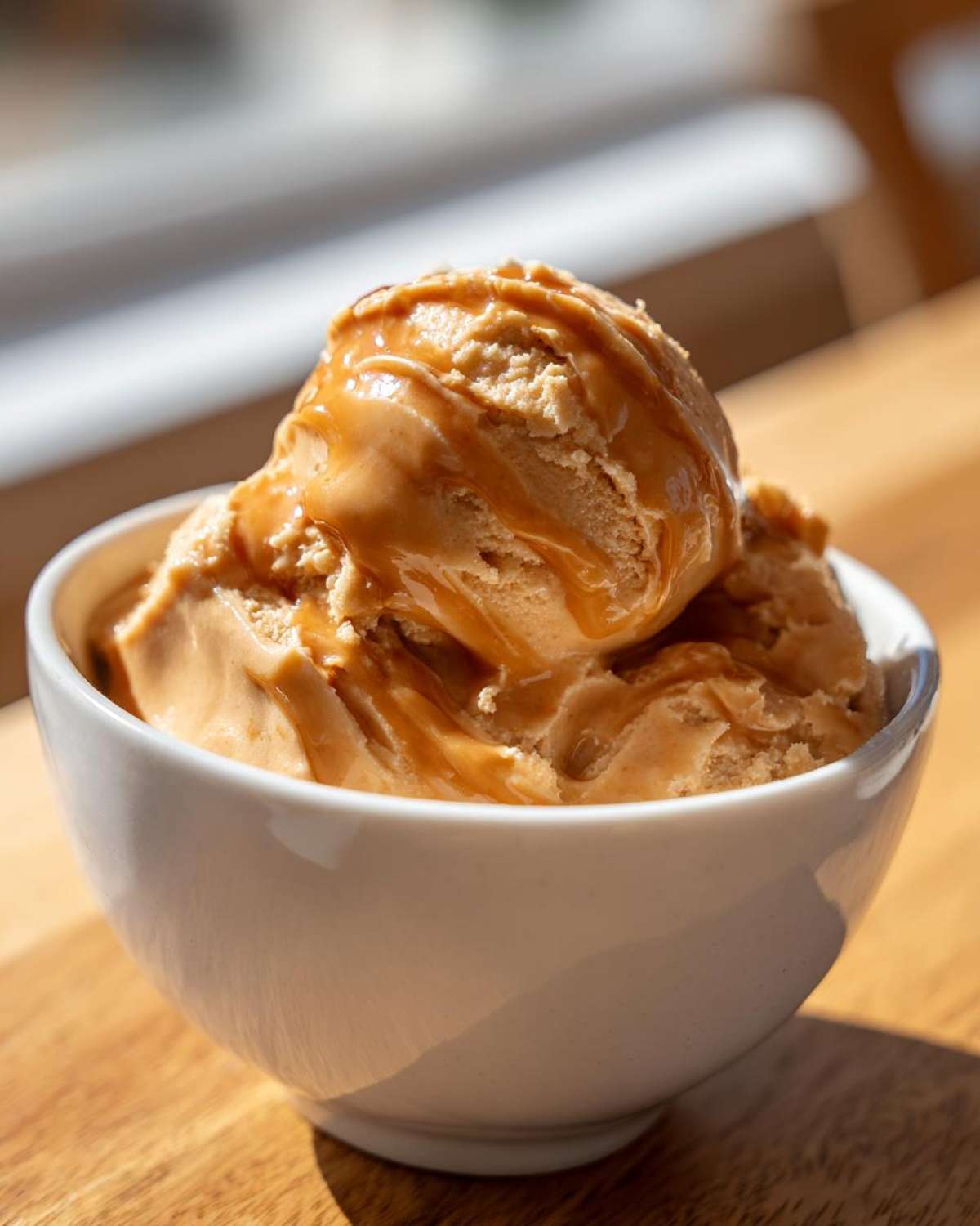 A bowl of caramel apple dip, drizzled with extra caramel, sitting on a wooden surface.