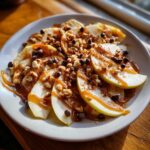 A plate of caramel apple nachos with sliced apples, caramel drizzle, chocolate chips, and chopped nuts.