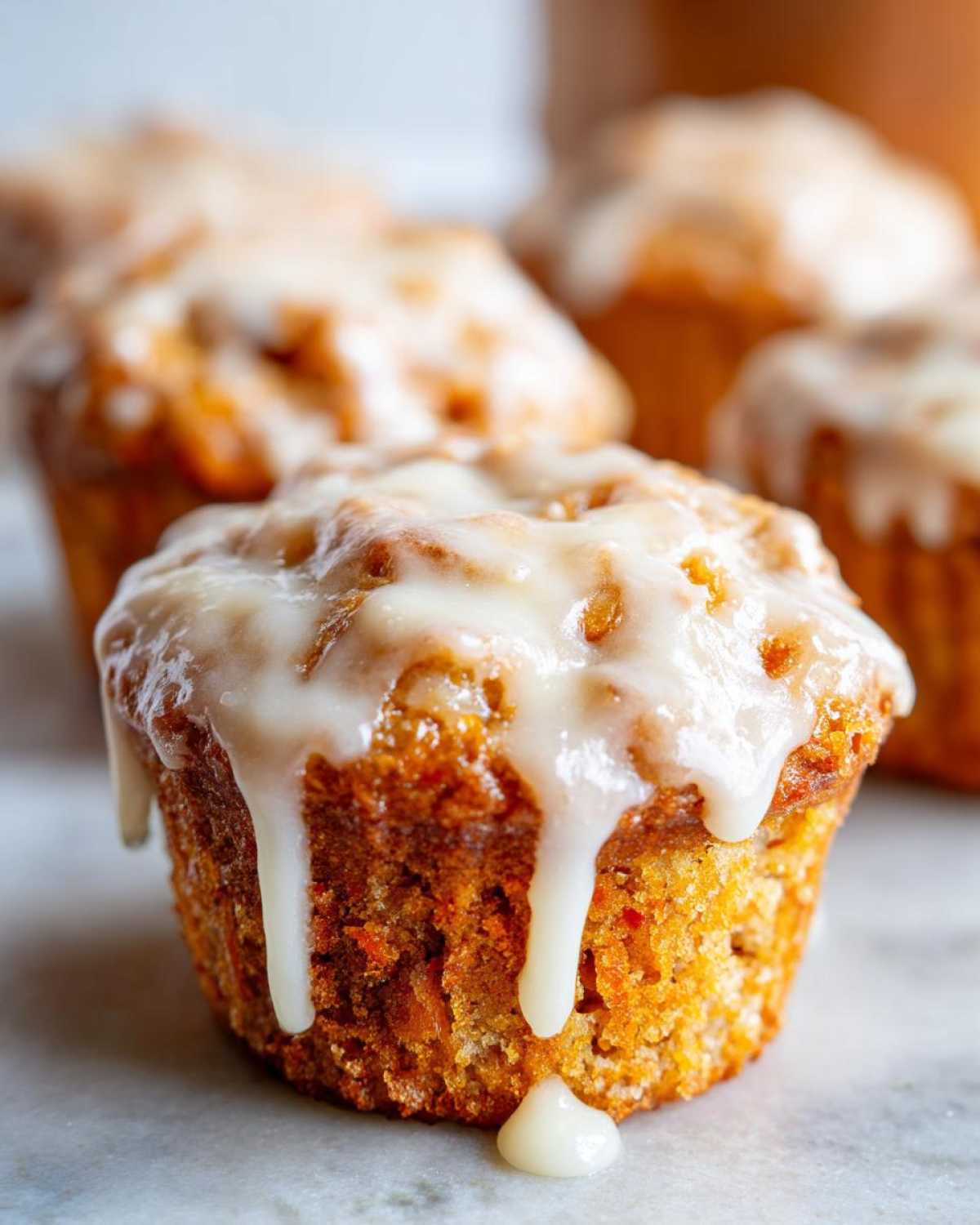 Close-up of a glazed carrot cake muffin with icing dripping down the sides.