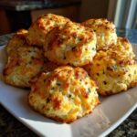 A stack of freshly baked Cheddar Bay Biscuits copycat on a white plate, golden brown and sprinkled with herbs.