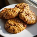 A plate of chewy maple cookies drizzled with maple glaze and topped with chopped pecans.
