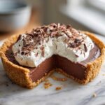 A decadent chocolate cream pie topped with whipped cream and chocolate shavings, with a slice removed.