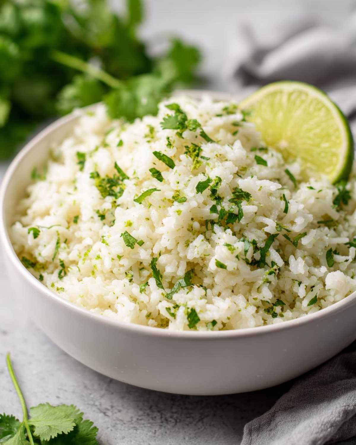 Close-up of a bowl of fluffy cilantro lime rice, a Chipotle copycat recipe, garnished with fresh cilantro and a lime wedge.