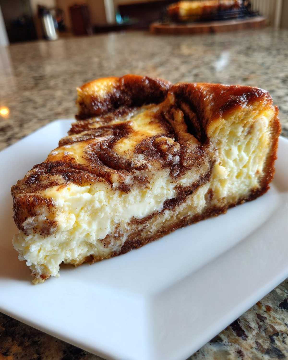 A delicious slice of cinnamon roll cheesecake on a white plate, showcasing the cinnamon swirl and creamy filling.