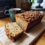A loaf of cinnamon streusel zucchini bread with a slice cut, served with a cup of coffee.