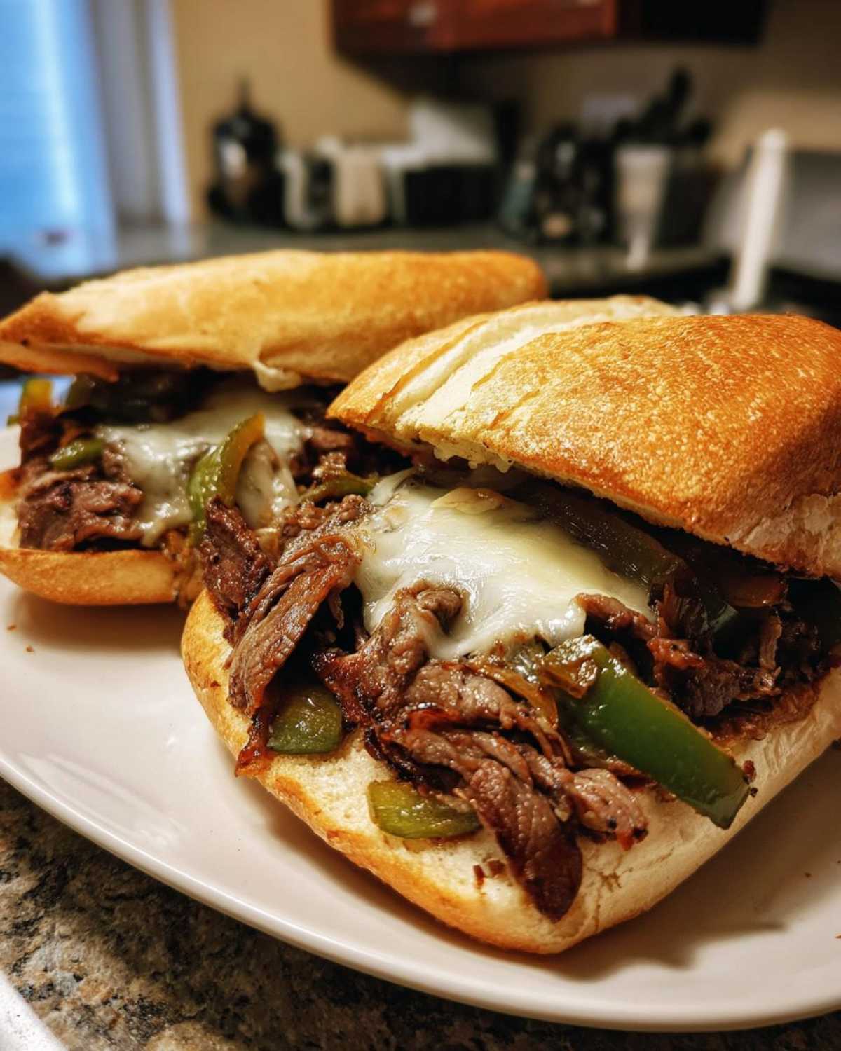 Two classic Philly cheesesteak sandwiches with melted cheese, steak, and peppers on a white plate.