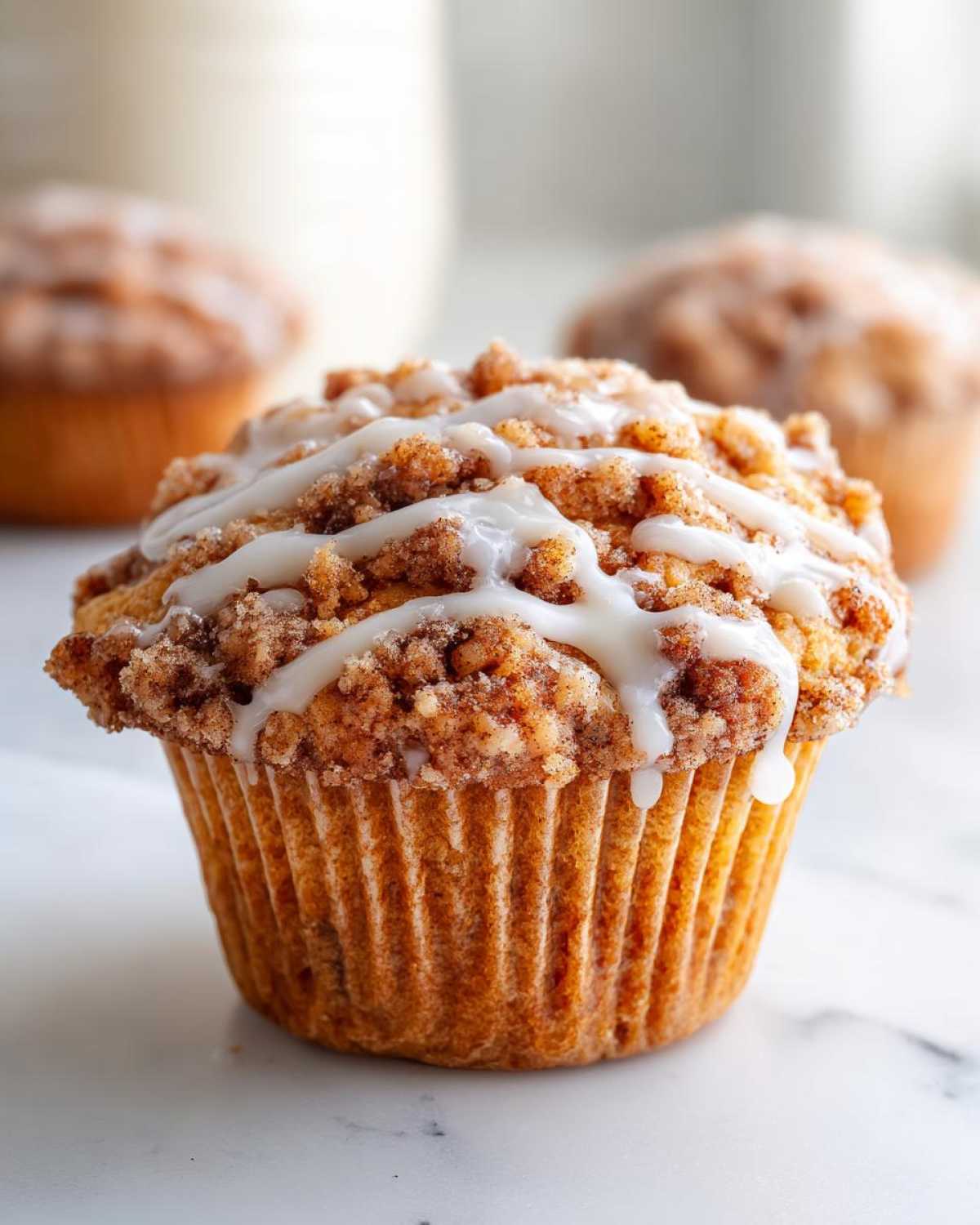 Close-up of a coffee cake muffin with streusel topping and a drizzle of white icing.
