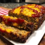 A slice of Cracker Barrel meatloaf copycat recipe, topped with ketchup and cheese, on a white plate.