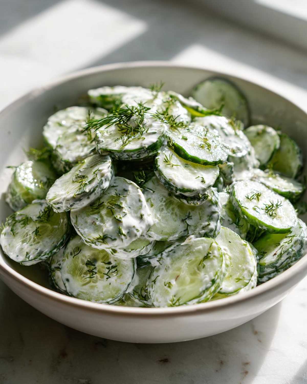 Close-up of creamy cucumber salad in a bowl, garnished with fresh dill.