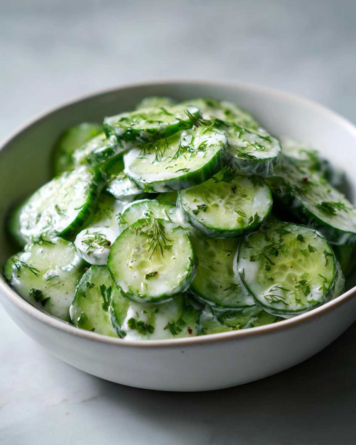 Close-up of a bowl filled with creamy cucumber salad, garnished with fresh dill.
