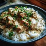 A delicious bowl of creamy smothered chicken and rice, garnished with fresh parsley.