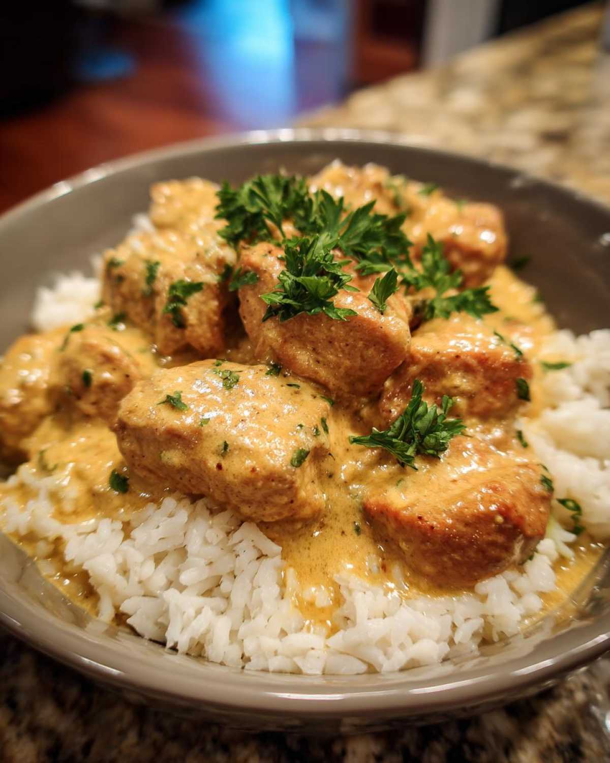 A bowl of creamy smothered chicken and rice, garnished with fresh parsley.