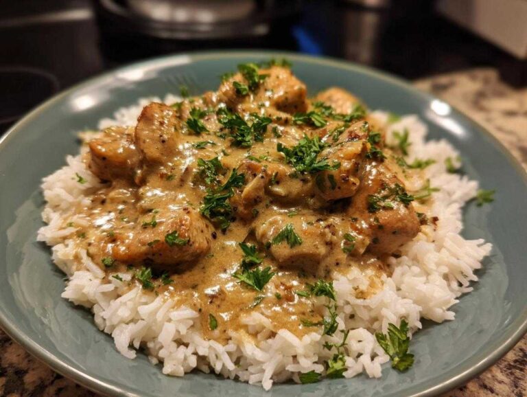 A plate of creamy smothered chicken and rice, garnished with fresh parsley.