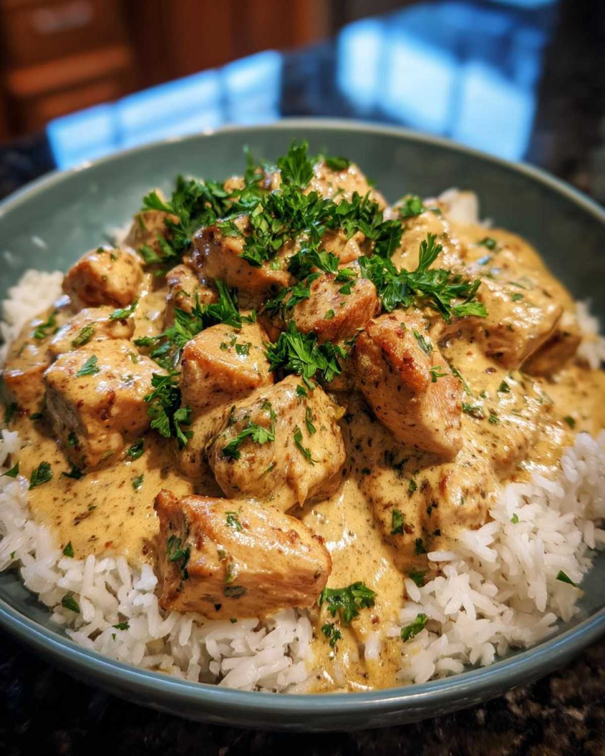 A bowl of creamy smothered chicken and rice, garnished with fresh parsley.