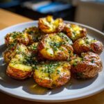 A plate of golden brown crispy smashed potatoes, topped with fresh herbs and glistening with oil.