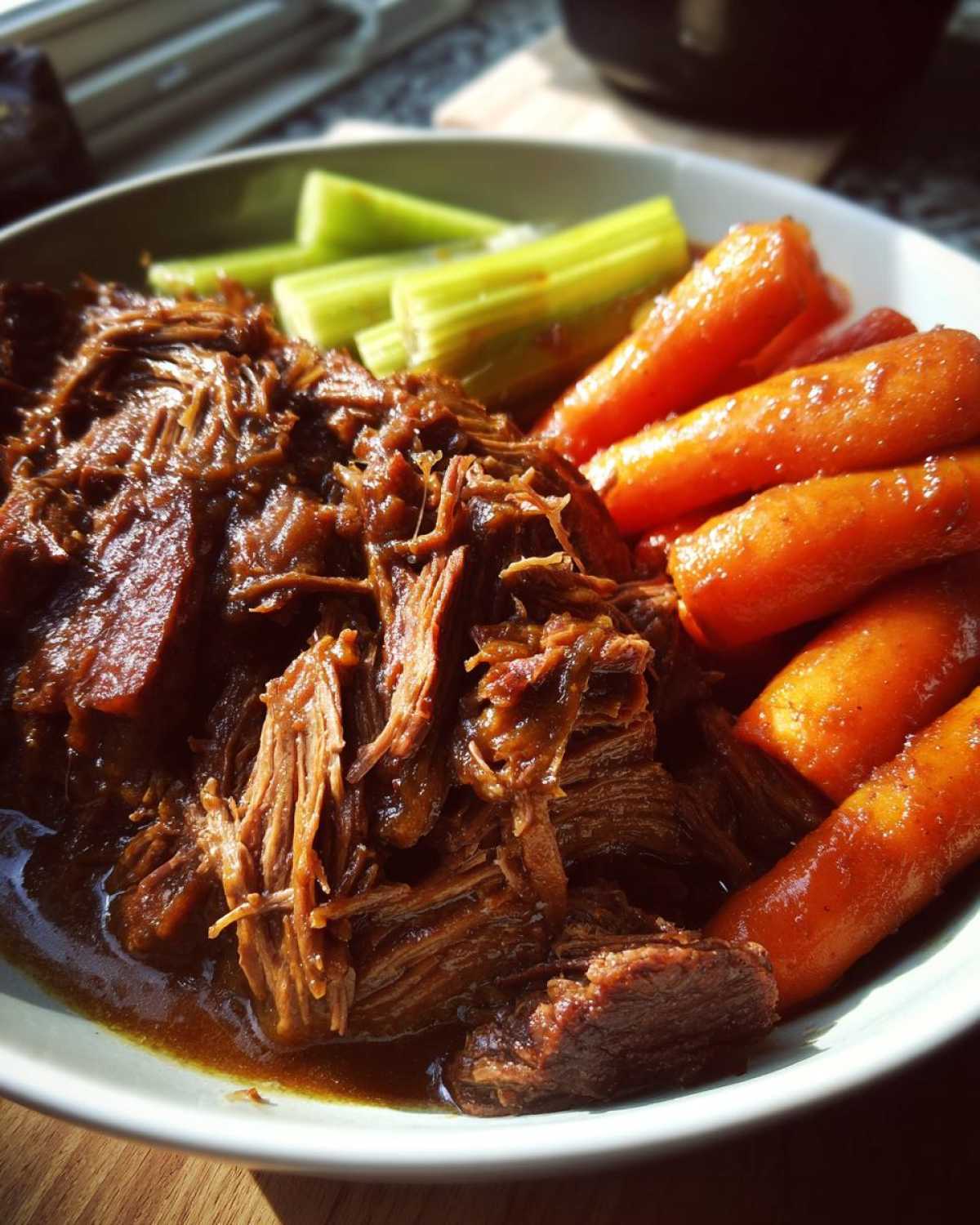 A plate of crockpot pot roast served with glazed carrots and celery sticks.
