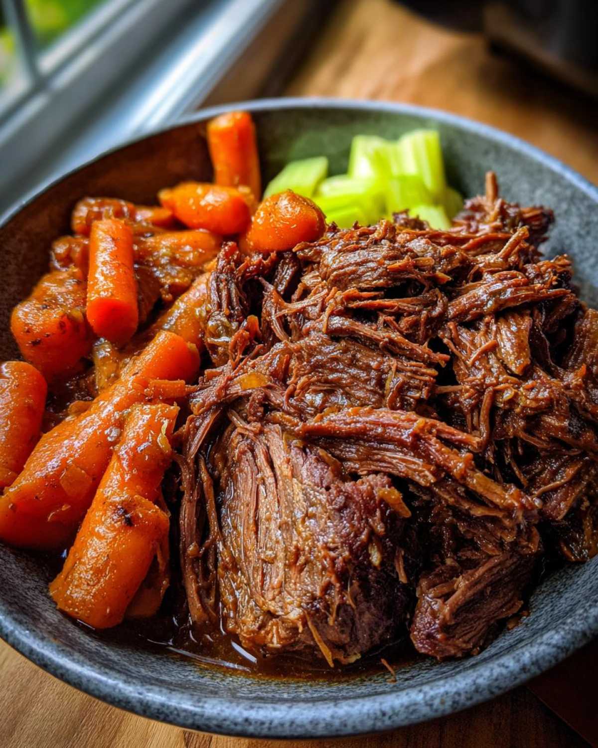 Close-up of crockpot pot roast in a bowl with carrots and celery, ready to serve.