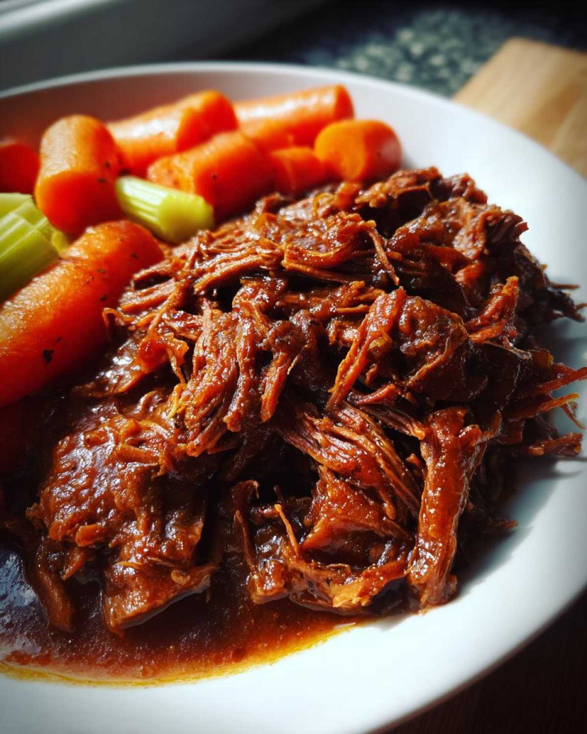 A plate of crockpot pot roast with carrots and celery, showcasing the tender, shredded beef.