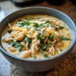 A bowl of creamy crockpot white chicken chili, topped with shredded chicken, white beans, cheese, and cilantro.