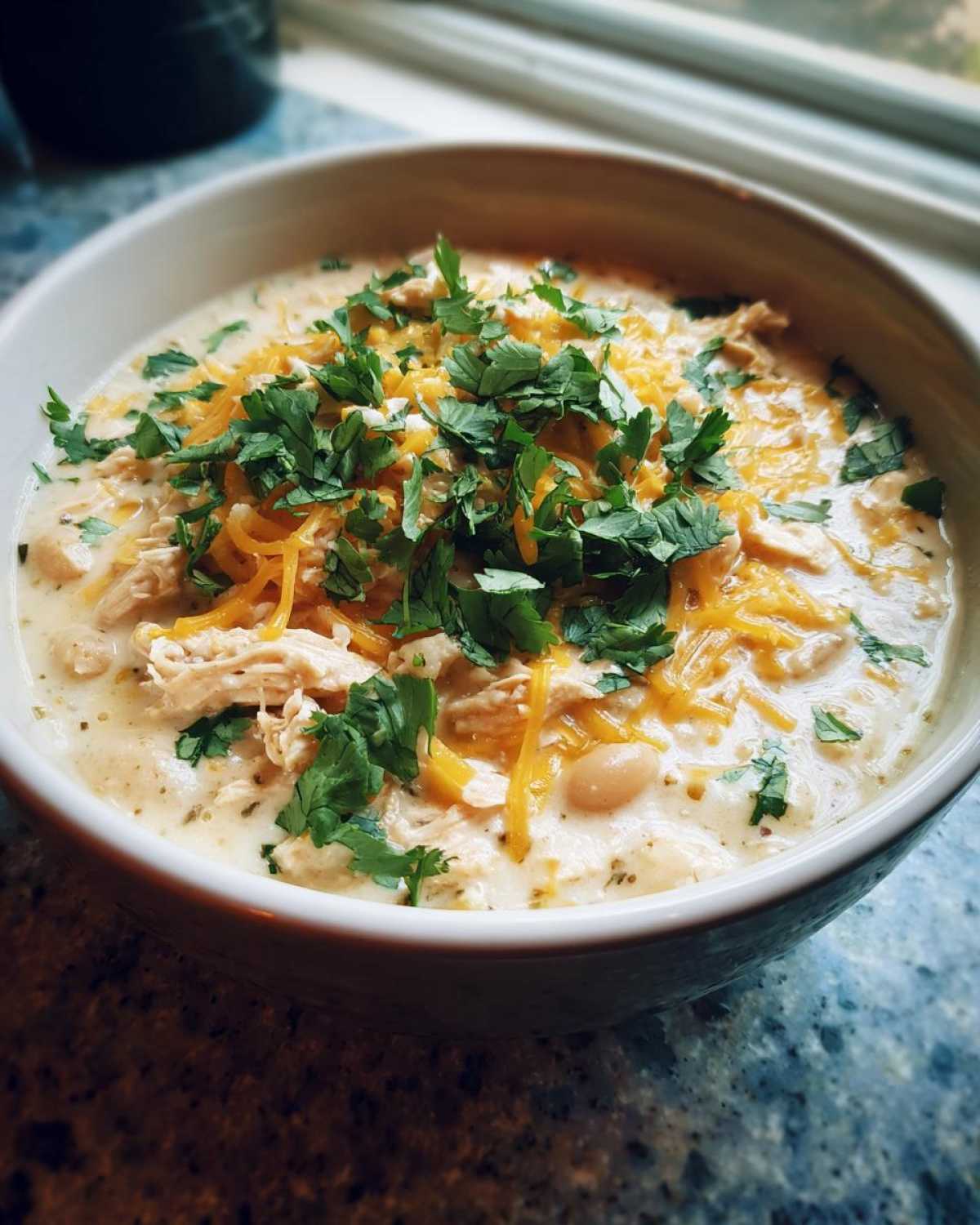 A comforting bowl of crockpot white chicken chili topped with cheese and fresh cilantro.