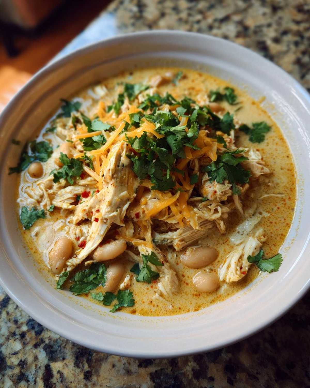 Overhead view of a bowl of crockpot white chicken chili, garnished with cheese and cilantro.