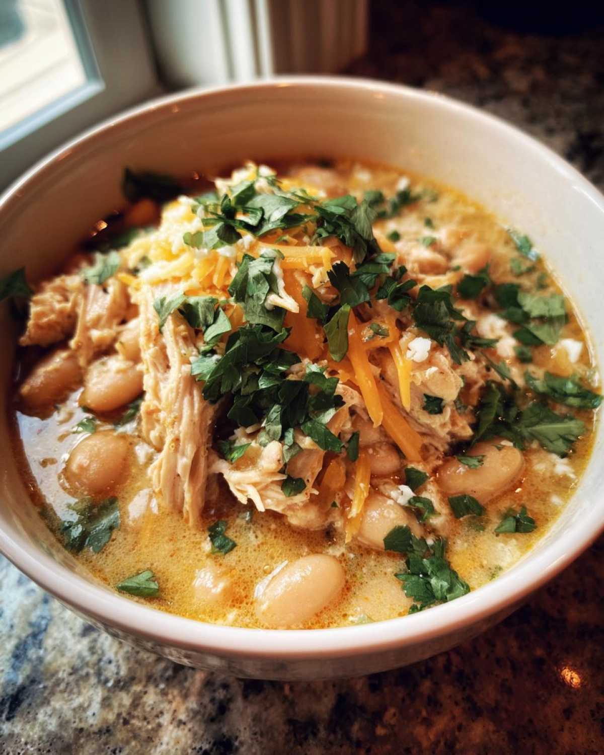 A delicious bowl of crockpot white chicken chili, topped with cheese and fresh parsley.