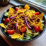 A vibrant bowl of Dorito taco salad with lettuce, seasoned meat, cheese, tomatoes, and Doritos.