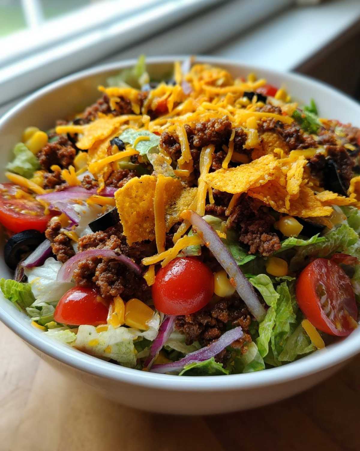 Close-up of a Dorito taco salad in a bowl, featuring lettuce, ground beef, tomatoes, cheese, and Doritos.