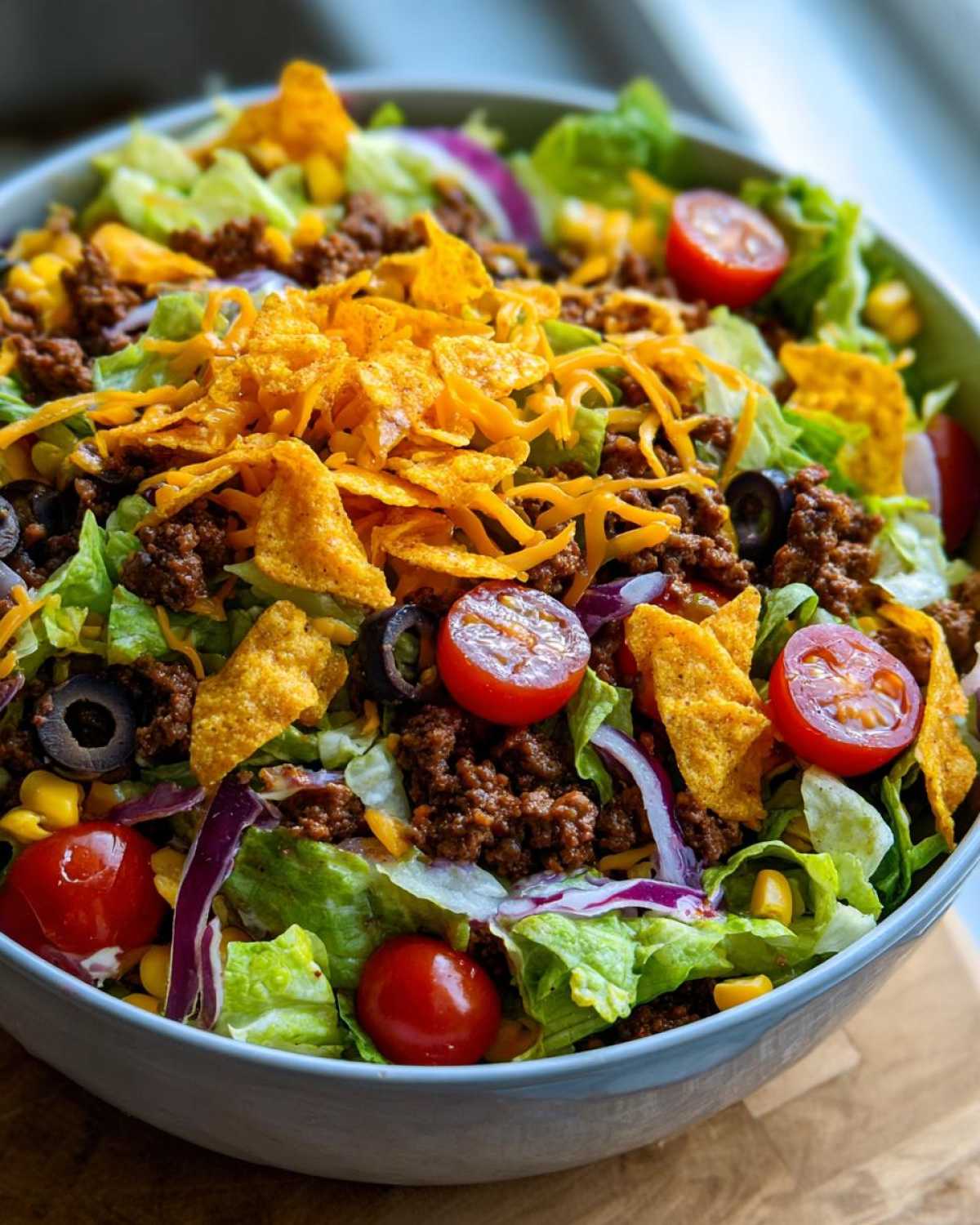 A vibrant bowl of Dorito taco salad with lettuce, ground beef, tomatoes, corn, olives, and Doritos.