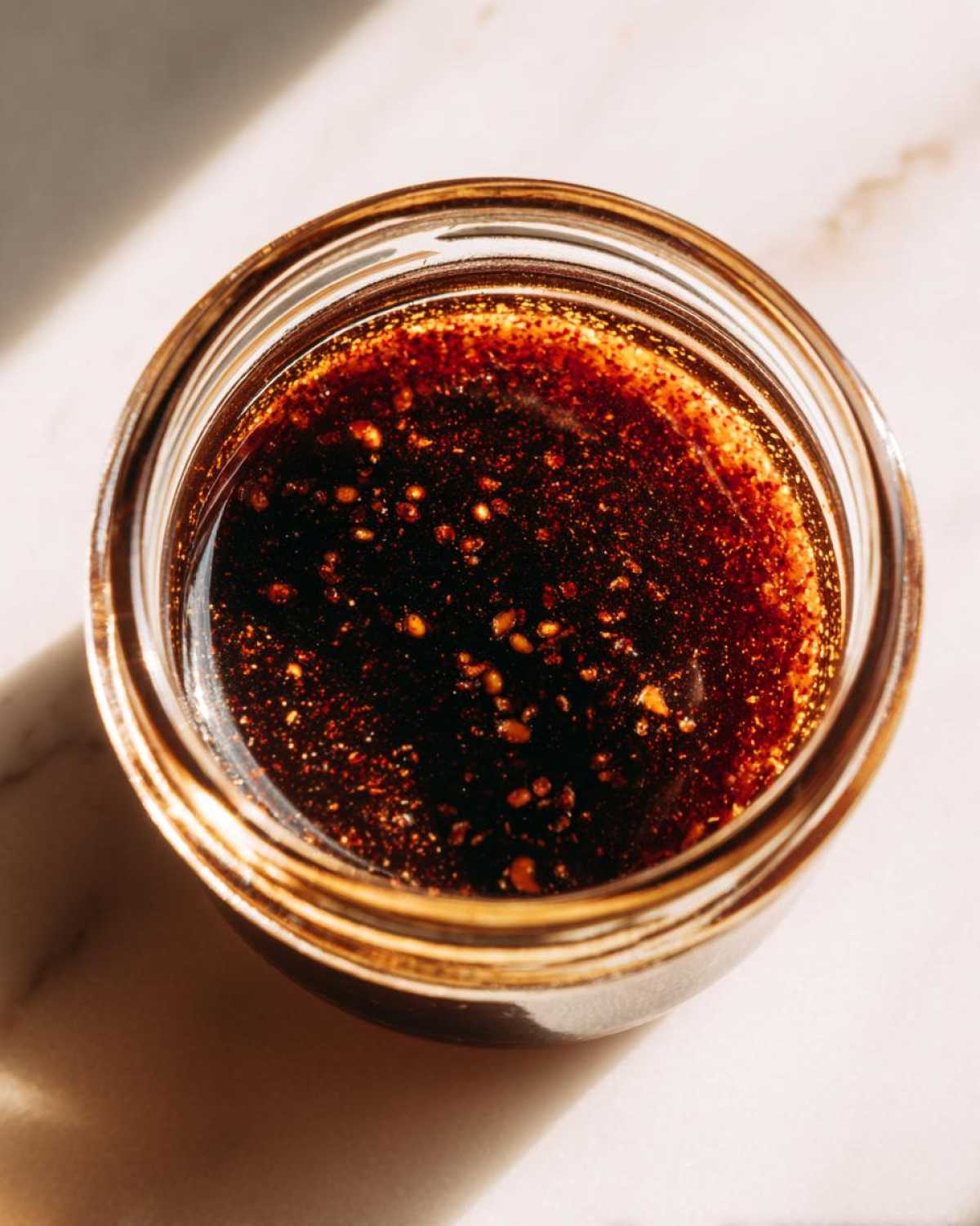 Overhead view of homemade dumpling sauce in a clear glass jar, showing sesame seeds and rich color.